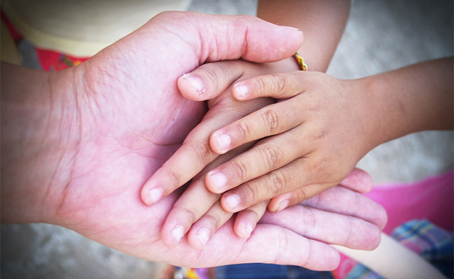 Foto di una mano di una persona adulta che stringe dolcemente le mani di due bambini
